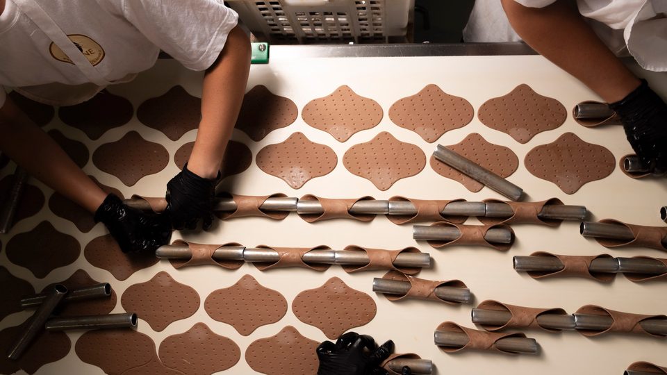 Porzioni di impasto avvolte a mano sugli stampi cilindrici per cannoli